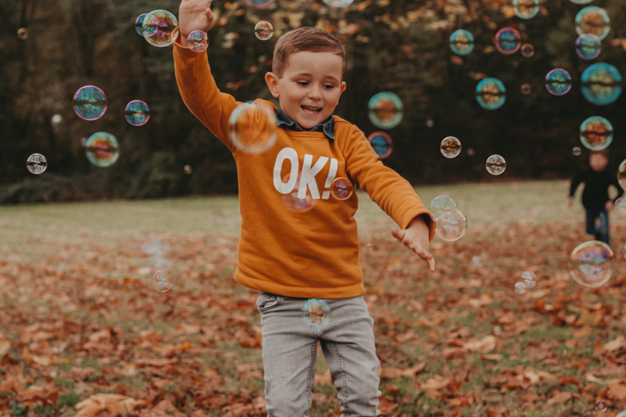Kleiner Junge mit orangenem Pulli läuft durch Seifenblasen